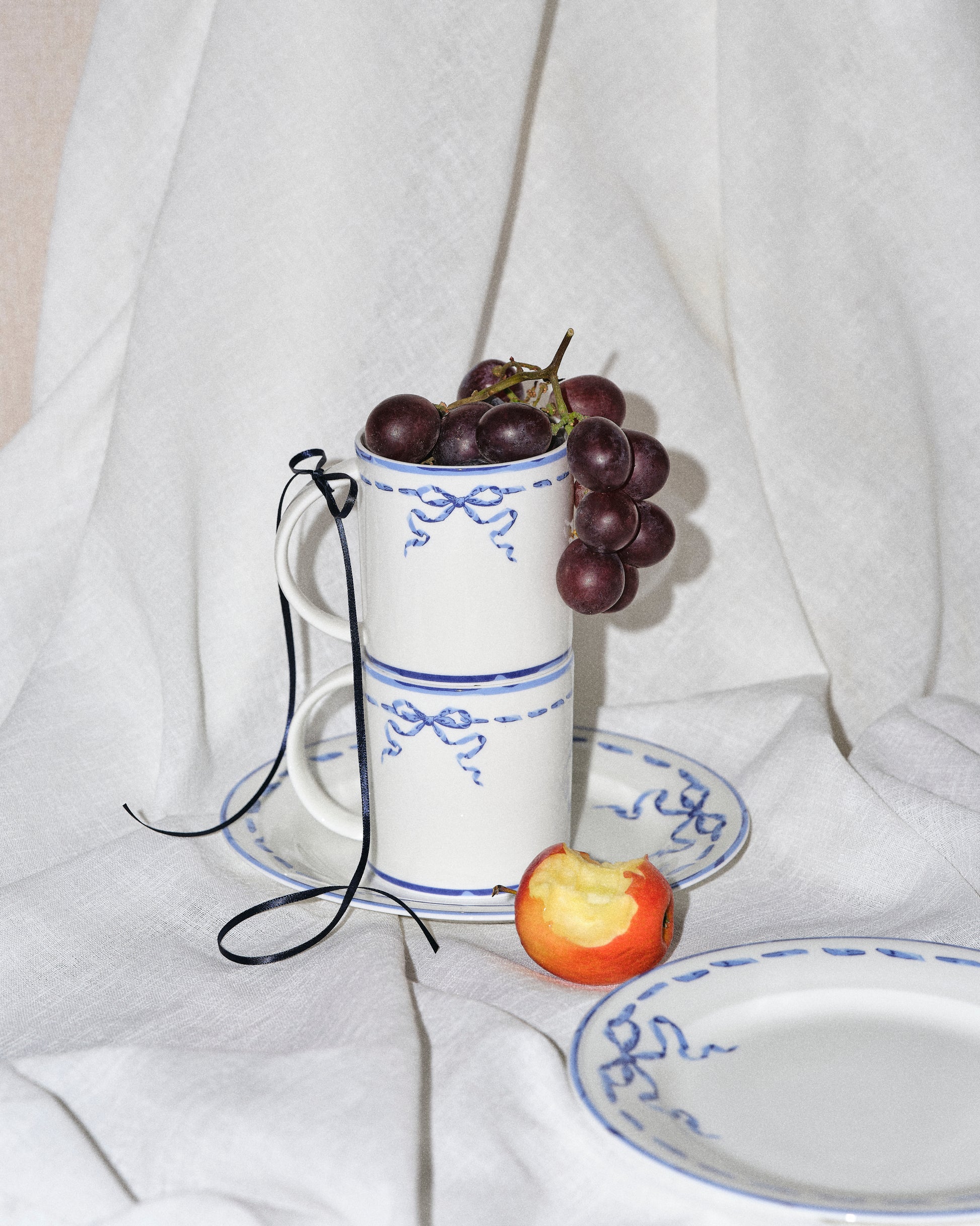 White ceramic cup with blue patterns filled with grapes on a white fabric background