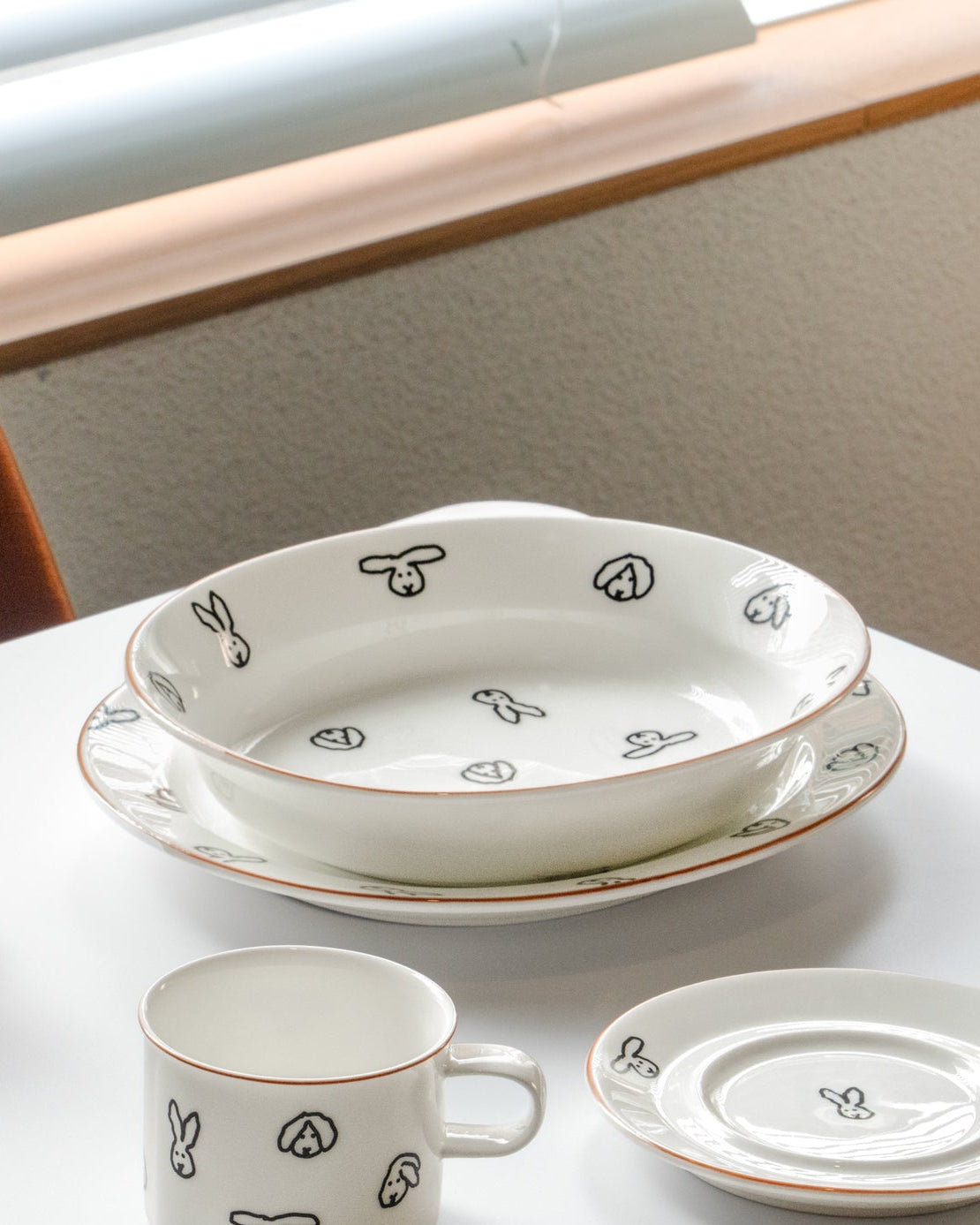 Ceramic tableware set on a white table with an orange chair.