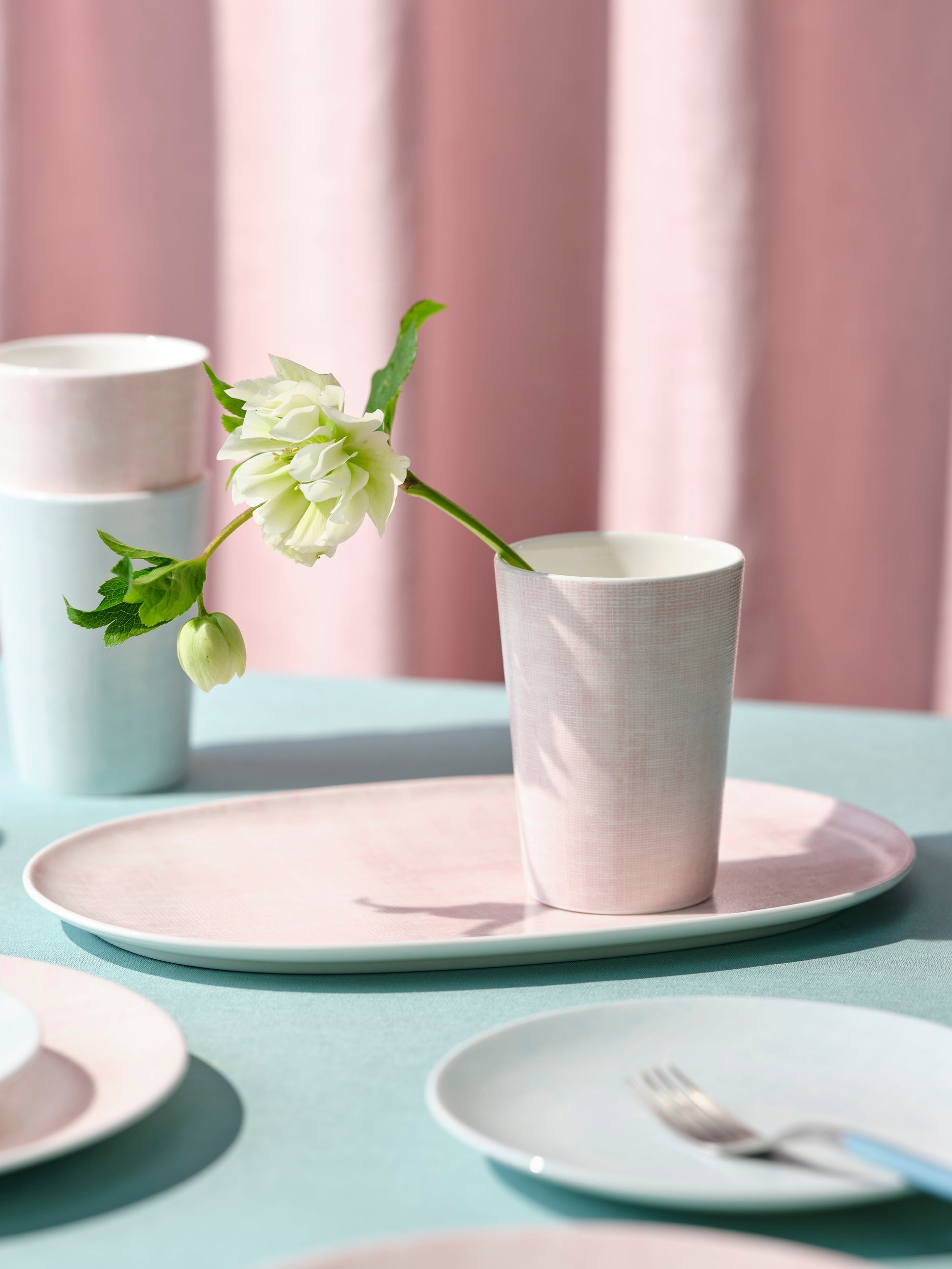 Table setting with pastel-colored plates and cups against a pink curtain background