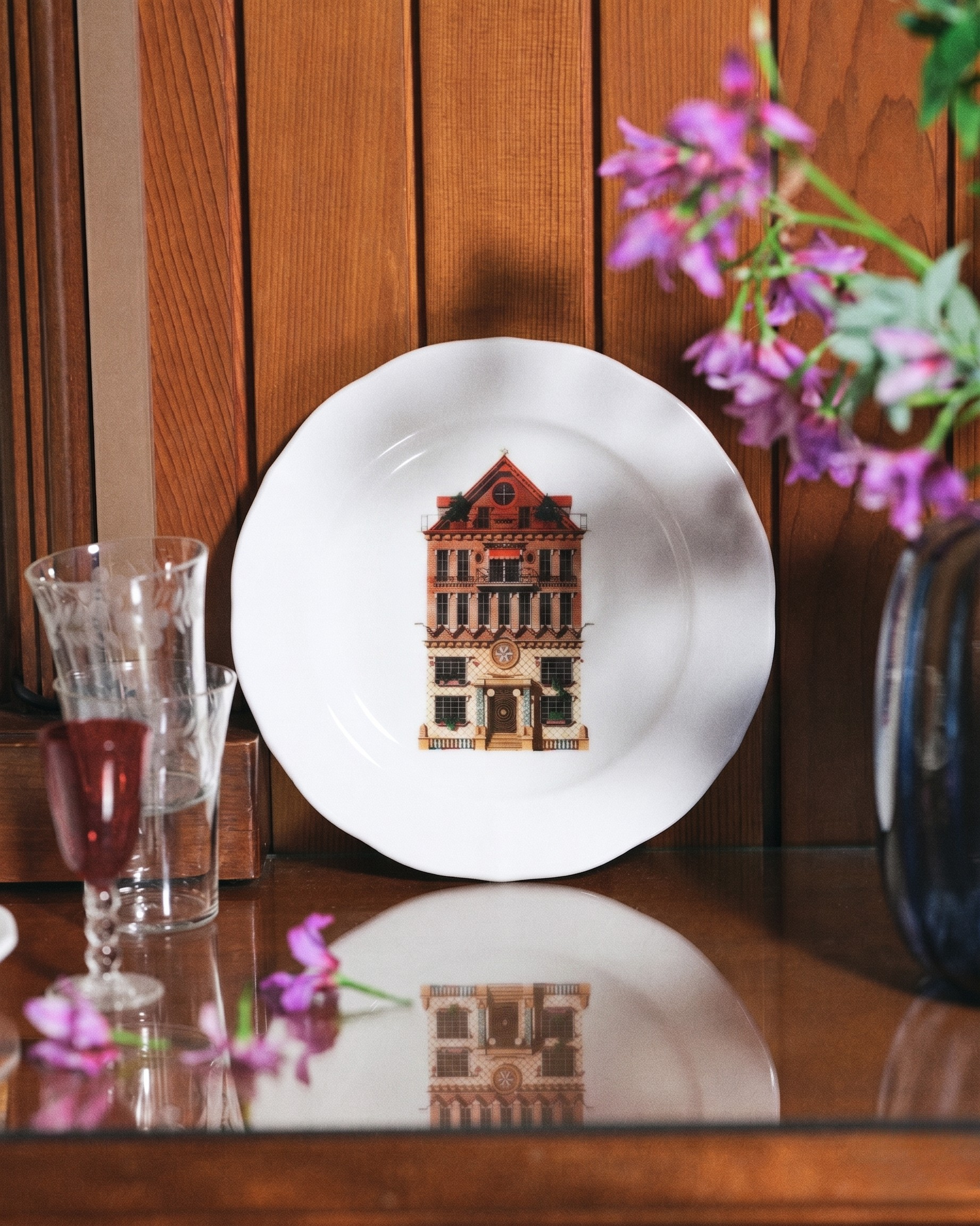 White plate with architectural design on a wooden surface with flowers and glasses.