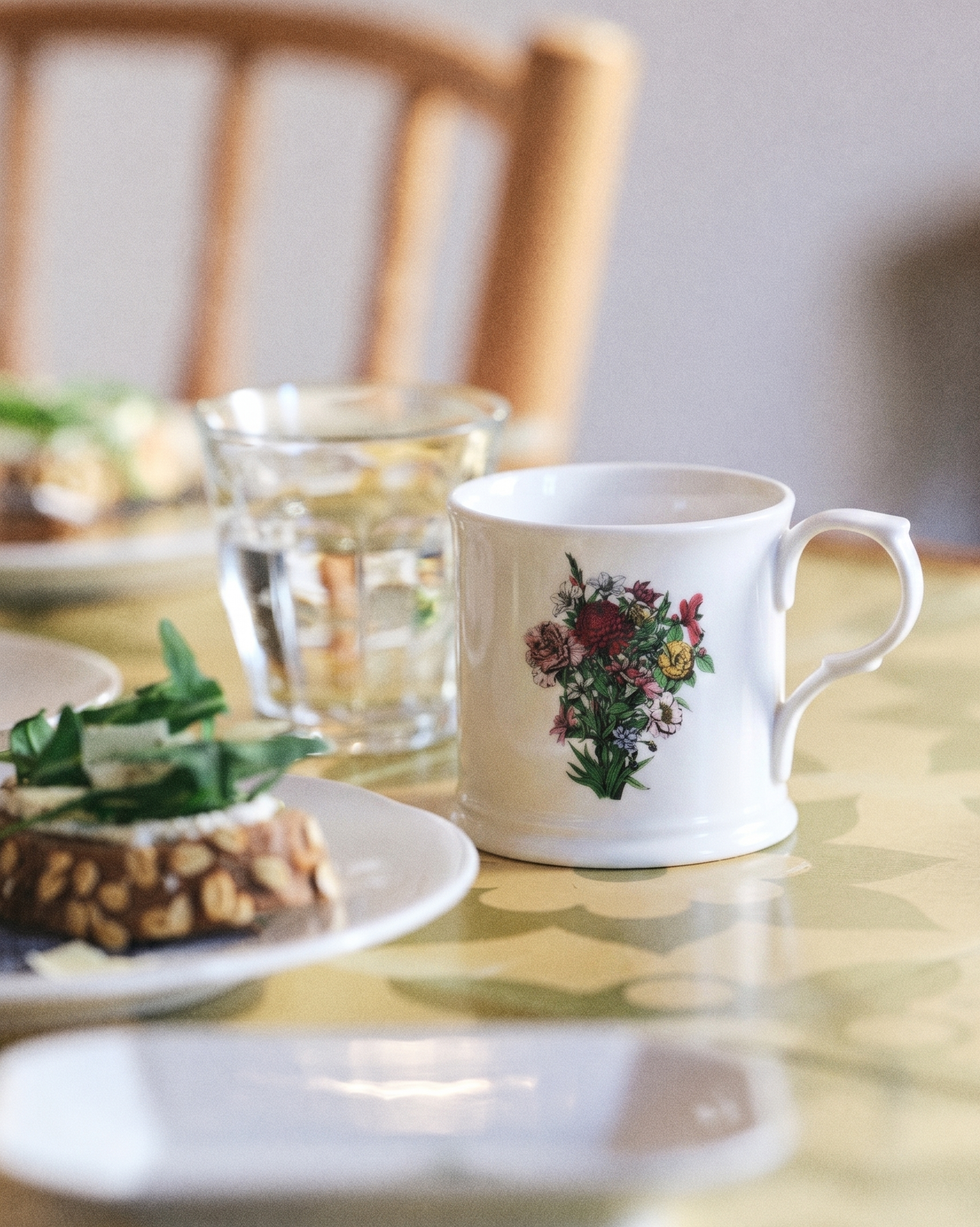 White mug with floral design on a table with food and glassware