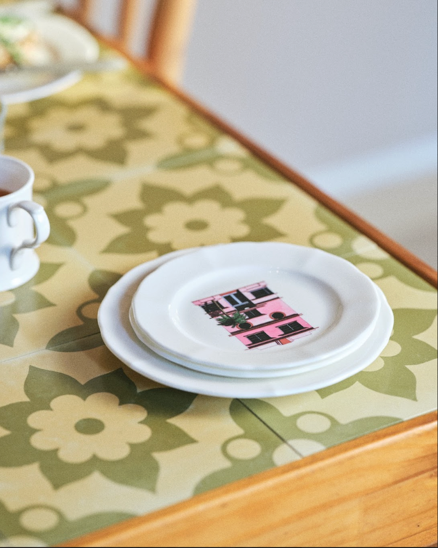 Stack of white plates with a pink and black design on a floral tablecloth.