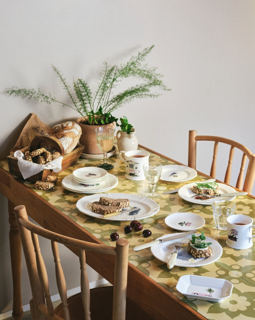 Dining table set with plates, cups, and food on a floral tablecloth.