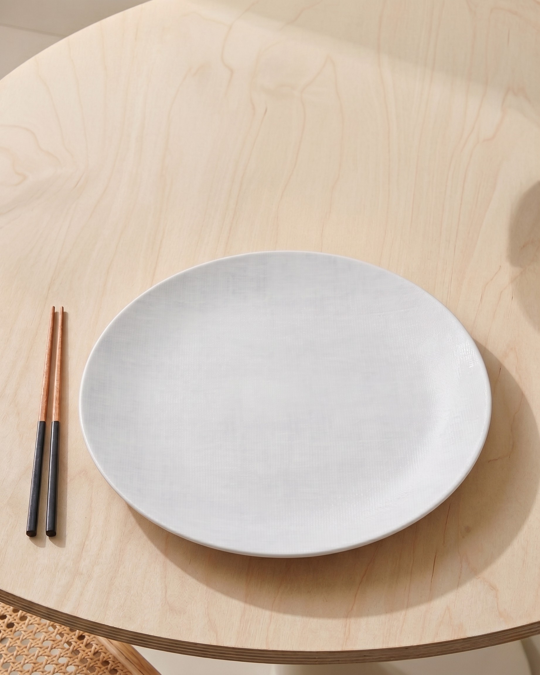White plate on a wooden table with two chopsticks.