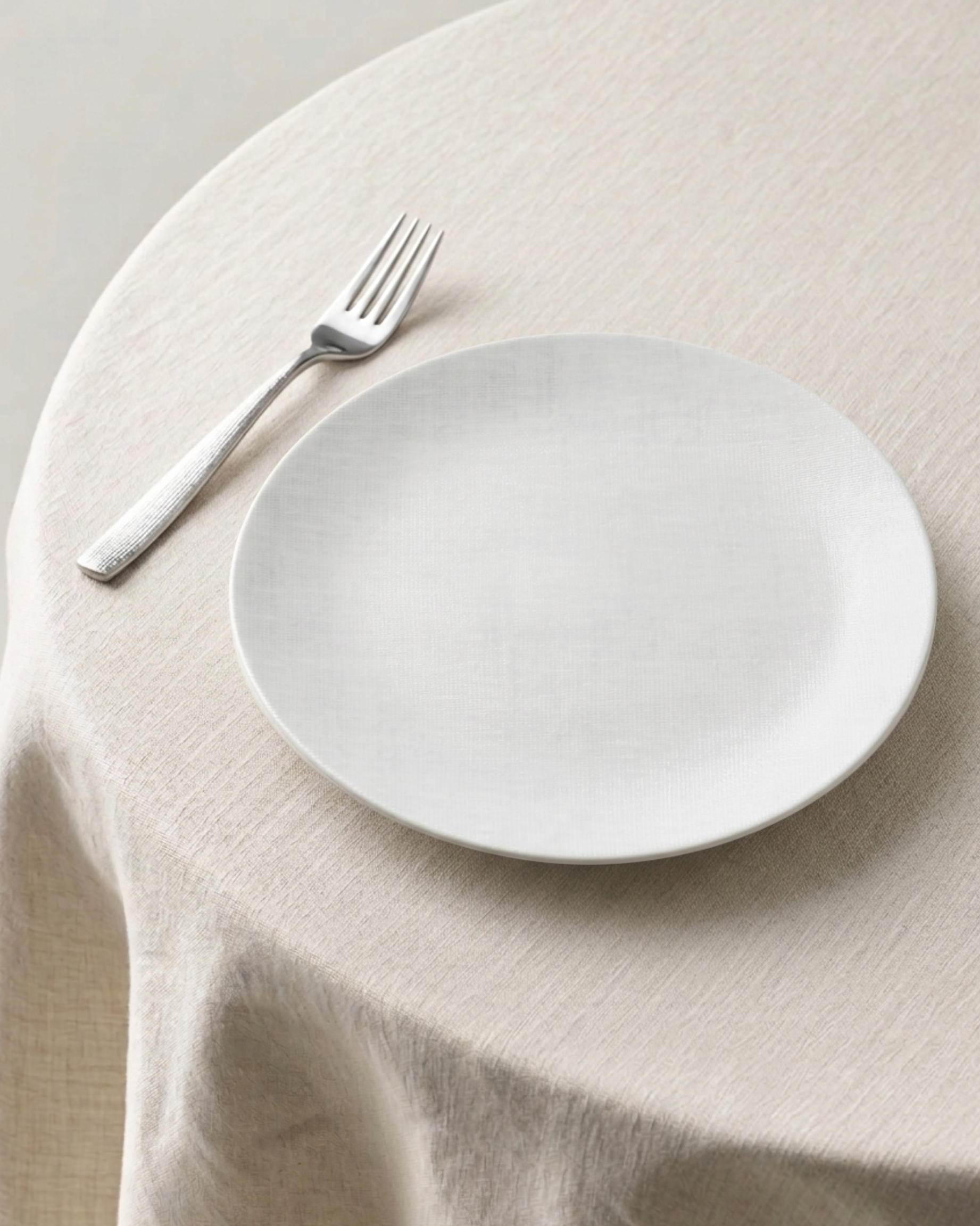 White plate and fork on a beige tablecloth