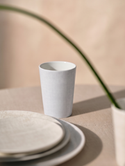 White ceramic cup and plates on a beige surface with a plant in the background