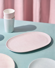 Pink ceramic plate and cups on a light blue surface with pink curtains in the background